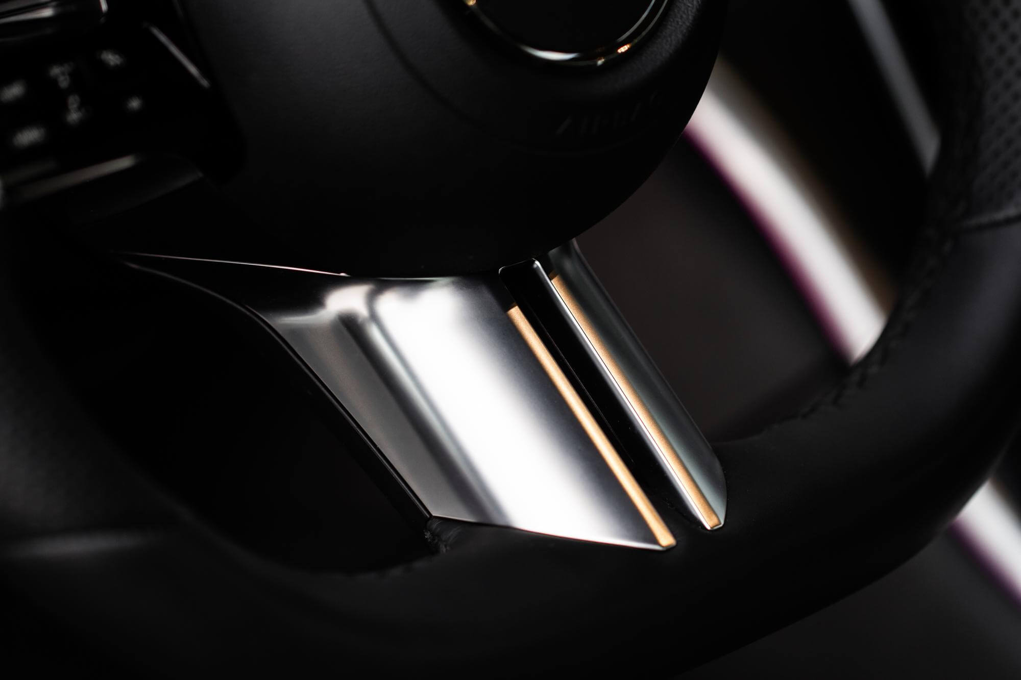 Lähikuva auton ohjauspyörästä, jossa on kromattu yksityiskohta ja musta nahkaverhoilu.